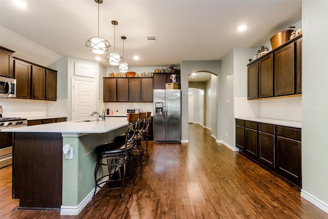 kitchen with decorative light fixtures, dark brown cabinetry, appliances with stainless steel finishes, and an island with sink