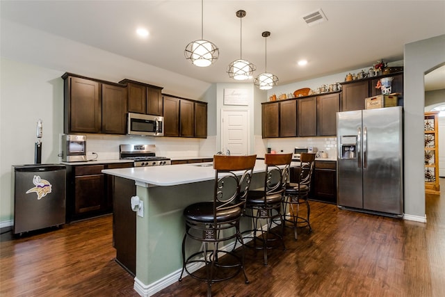 kitchen with dark wood-type flooring, appliances with stainless steel finishes, dark brown cabinetry, and hanging light fixtures