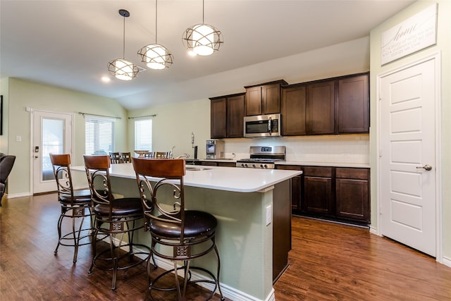 kitchen featuring appliances with stainless steel finishes, a kitchen island with sink, decorative light fixtures, dark brown cabinets, and vaulted ceiling