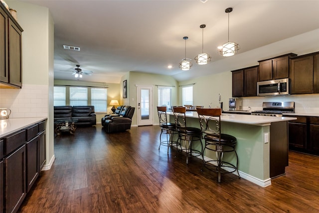 kitchen with tasteful backsplash, a kitchen island, dark brown cabinetry, appliances with stainless steel finishes, and a breakfast bar area