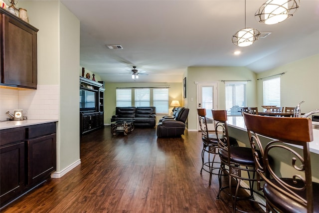 interior space with ceiling fan, dark hardwood / wood-style floors, tasteful backsplash, dark brown cabinets, and pendant lighting