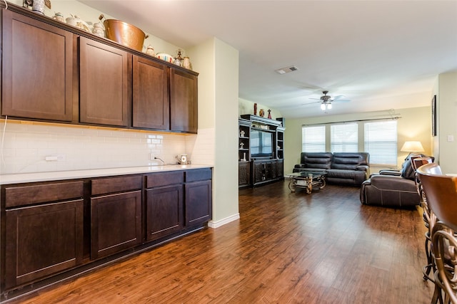 kitchen with ceiling fan, dark wood-type flooring, dark brown cabinets, and tasteful backsplash