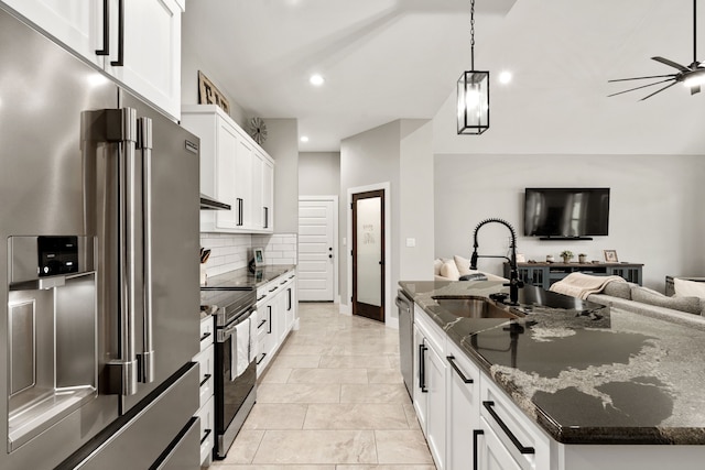 kitchen featuring dark stone countertops, stainless steel appliances, an island with sink, white cabinets, and decorative light fixtures