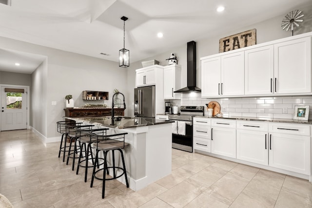 kitchen featuring white cabinets, a center island with sink, appliances with stainless steel finishes, and wall chimney exhaust hood