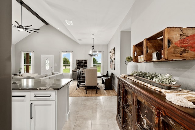 kitchen featuring hanging light fixtures, high vaulted ceiling, ceiling fan with notable chandelier, white cabinets, and dark stone counters