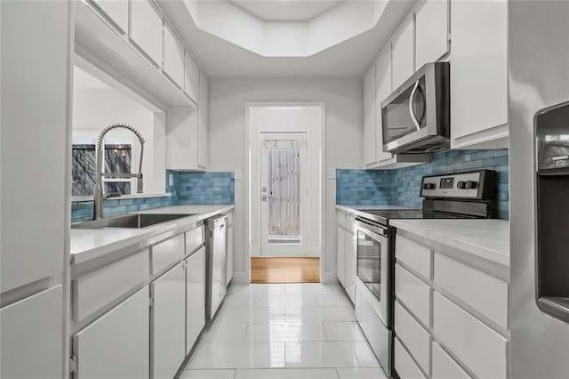 kitchen with a raised ceiling, stainless steel appliances, sink, white cabinetry, and tasteful backsplash