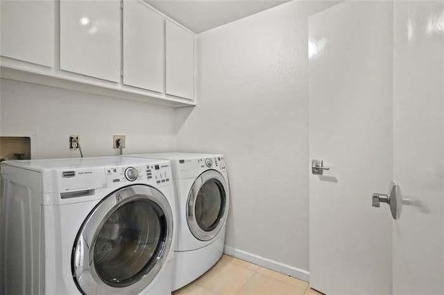 laundry room featuring washing machine and dryer, light tile patterned floors, and cabinets