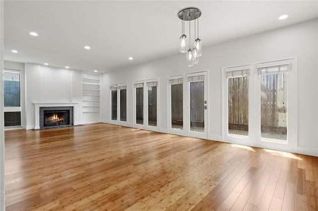 unfurnished living room featuring a chandelier, built in shelves, and wood-type flooring