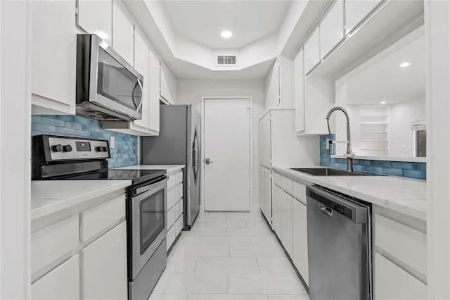 kitchen featuring stainless steel appliances, sink, white cabinetry, backsplash, and a tray ceiling