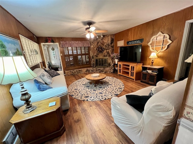 living room with a fireplace, ceiling fan, light wood-type flooring, and wood walls