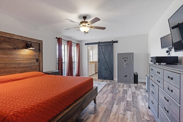 bedroom with a textured ceiling, connected bathroom, light hardwood / wood-style floors, ceiling fan, and a barn door