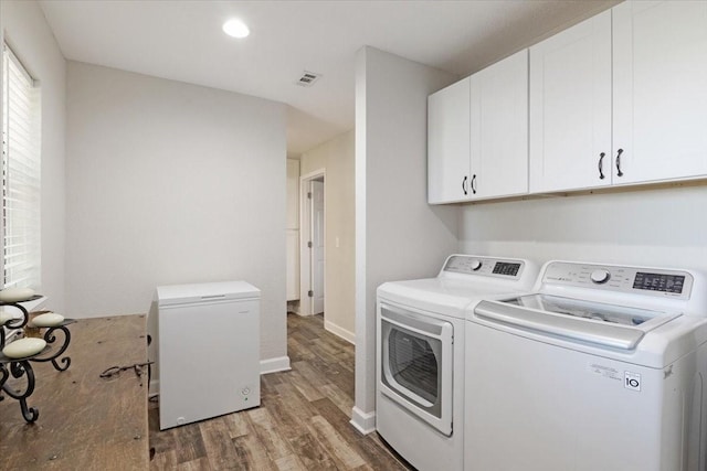 clothes washing area featuring cabinets, hardwood / wood-style floors, and washing machine and clothes dryer