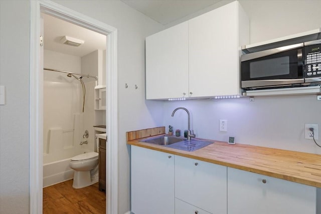 kitchen with white cabinetry, butcher block counters, hardwood / wood-style flooring, and sink