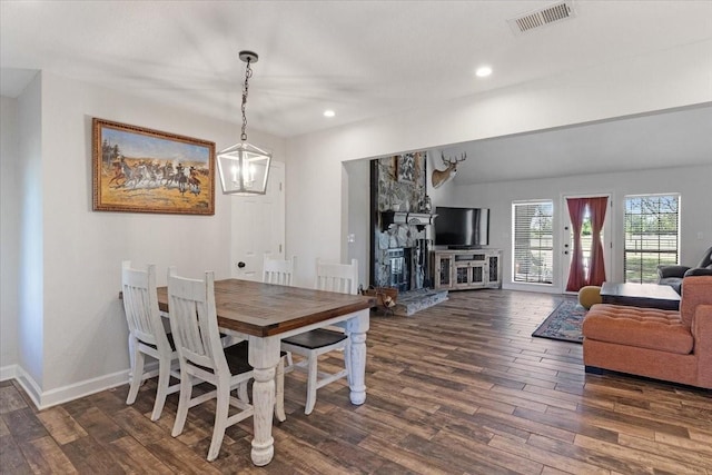 dining area with dark hardwood / wood-style floors, a notable chandelier, and a stone fireplace