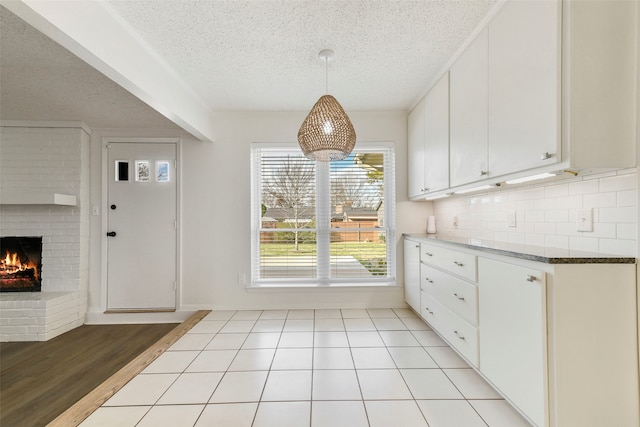 kitchen with a brick fireplace, decorative backsplash, pendant lighting, and white cabinets