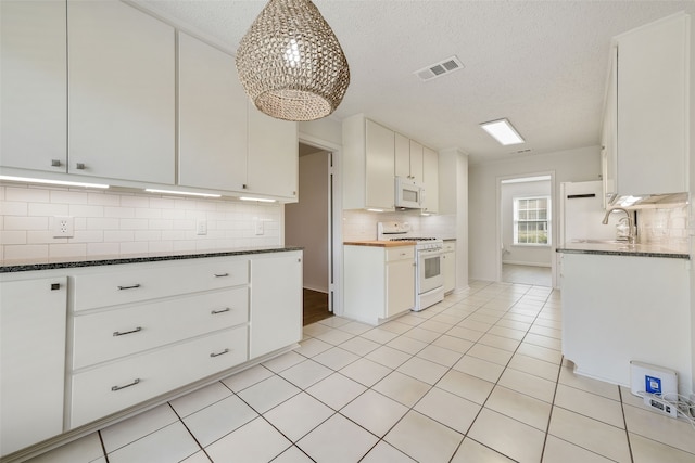 kitchen with white appliances, white cabinets, a textured ceiling, dark stone countertops, and sink