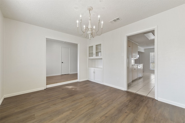 empty room with built in shelves, a textured ceiling, a chandelier, and light hardwood / wood-style floors