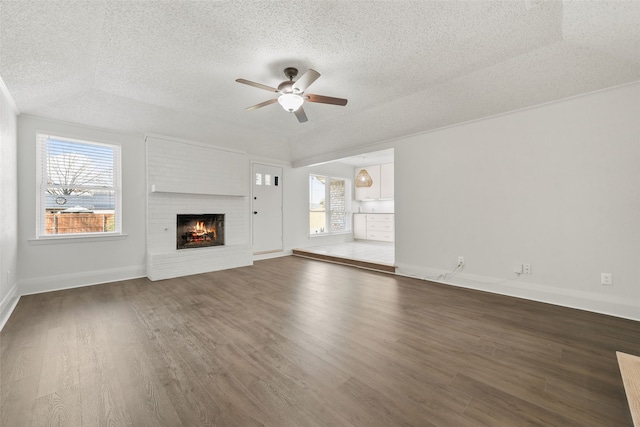 unfurnished living room with a brick fireplace, a healthy amount of sunlight, dark hardwood / wood-style floors, and ceiling fan