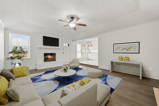 living room featuring a brick fireplace, a healthy amount of sunlight, hardwood / wood-style flooring, and ceiling fan