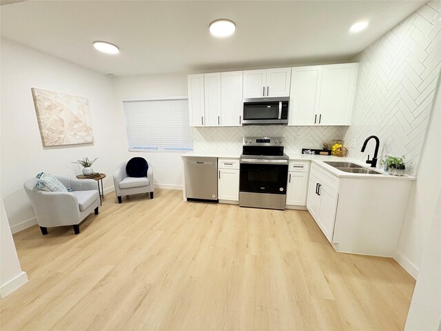 kitchen with light hardwood / wood-style floors, stainless steel appliances, decorative backsplash, sink, and white cabinetry