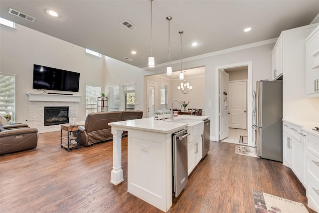 kitchen featuring stainless steel appliances, a center island with sink, white cabinets, and hanging light fixtures