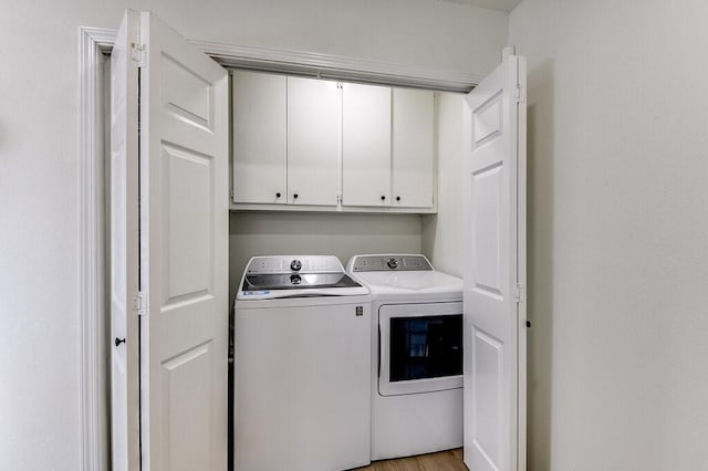 laundry room with washing machine and dryer, cabinets, and light hardwood / wood-style flooring