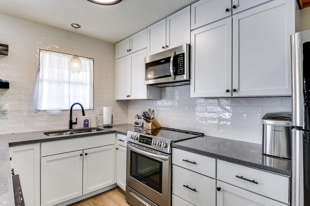 kitchen with stainless steel appliances, sink, white cabinetry, tasteful backsplash, and hanging light fixtures