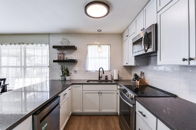 kitchen with dark stone countertops, appliances with stainless steel finishes, white cabinets, decorative light fixtures, and sink