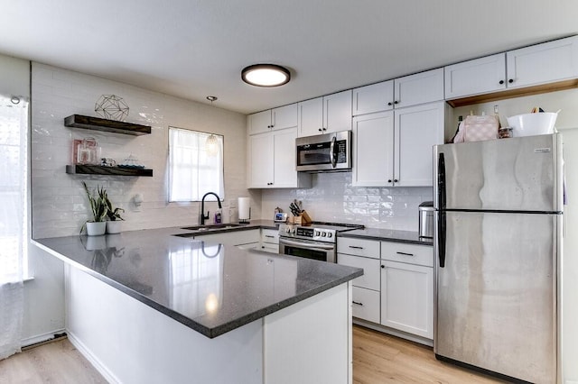 kitchen featuring appliances with stainless steel finishes, white cabinetry, light wood-type flooring, and kitchen peninsula