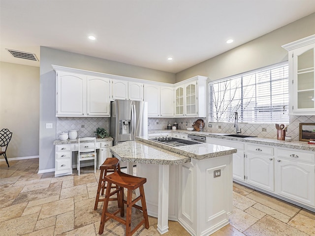 kitchen with a kitchen breakfast bar, a center island, stainless steel refrigerator with ice dispenser, white cabinets, and sink