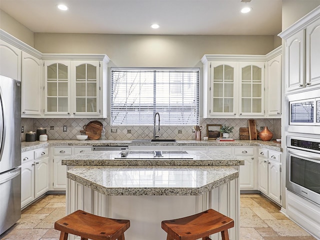 kitchen with backsplash, stainless steel appliances, white cabinets, and a kitchen bar