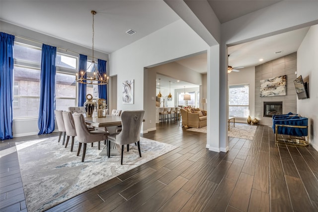 dining room featuring ceiling fan with notable chandelier, a large fireplace, and a healthy amount of sunlight