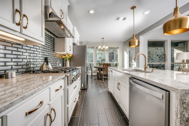 kitchen with pendant lighting, stainless steel appliances, wall chimney range hood, white cabinets, and sink