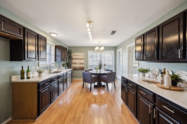 kitchen with a chandelier, light hardwood / wood-style floors, hanging light fixtures, dark brown cabinetry, and sink