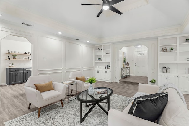 living room featuring light hardwood / wood-style floors, ceiling fan, crown molding, and built in shelves