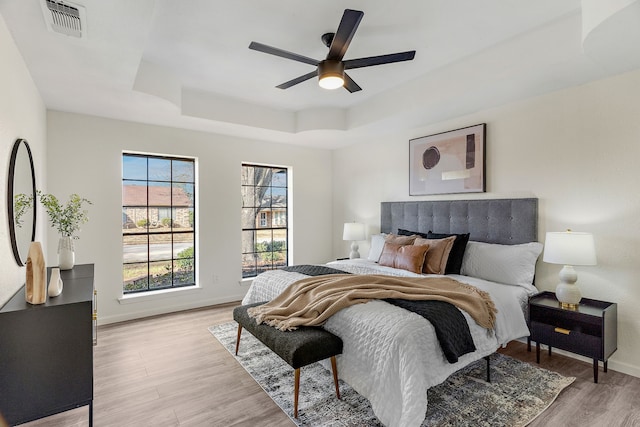 bedroom with light wood-type flooring, ceiling fan, and a tray ceiling