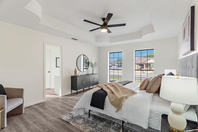 bedroom featuring ceiling fan, light hardwood / wood-style floors, and a tray ceiling