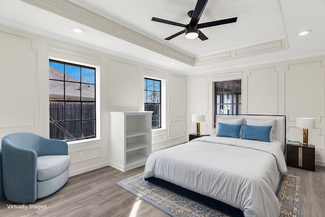 bedroom with ornamental molding, ceiling fan, a tray ceiling, and light wood-type flooring