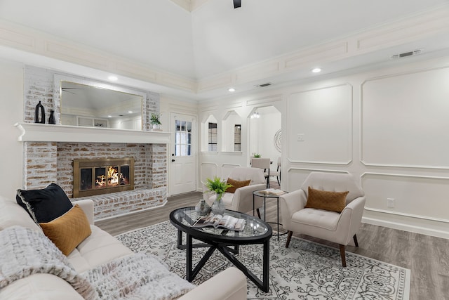 living room with a brick fireplace, hardwood / wood-style floors, ceiling fan, and ornamental molding