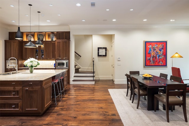 kitchen with sink, decorative light fixtures, light stone countertops, dark hardwood / wood-style flooring, and stainless steel microwave