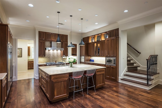 kitchen with appliances with stainless steel finishes, decorative light fixtures, backsplash, a kitchen island with sink, and dark wood-type flooring