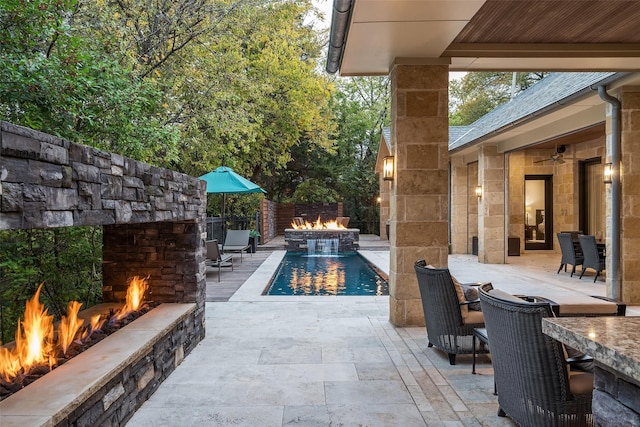 view of pool with a patio, a fire pit, pool water feature, and an outdoor stone fireplace