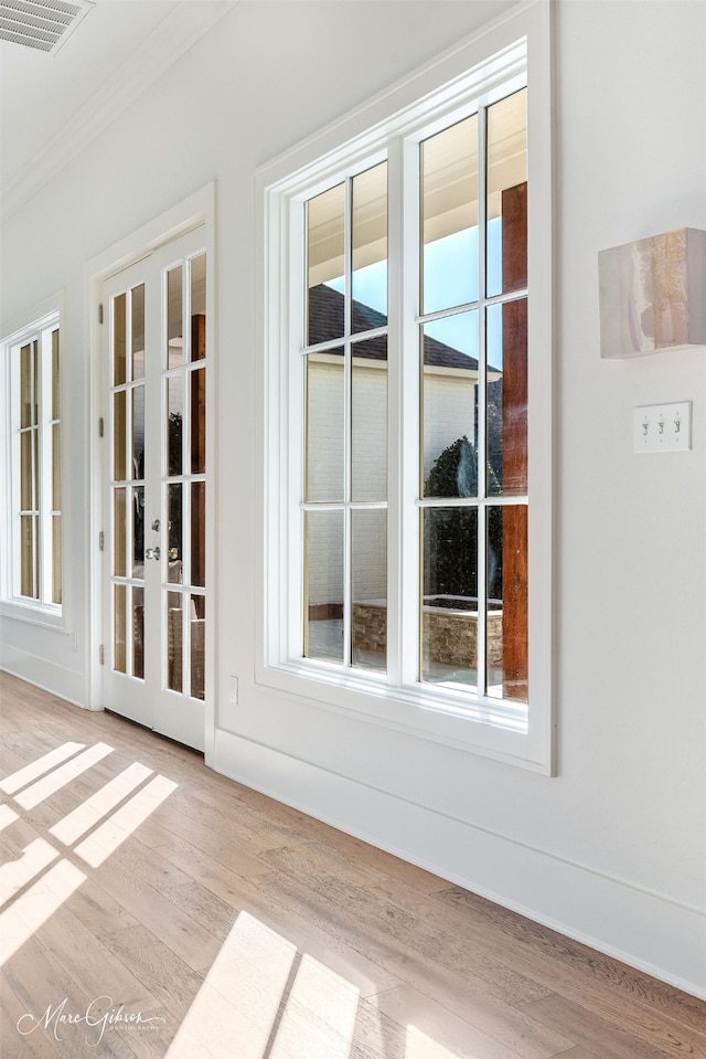 interior space featuring ornamental molding, light wood-type flooring, french doors, and plenty of natural light