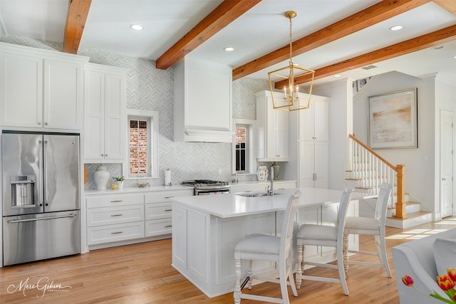 kitchen featuring a kitchen island with sink, stainless steel appliances, pendant lighting, white cabinets, and sink