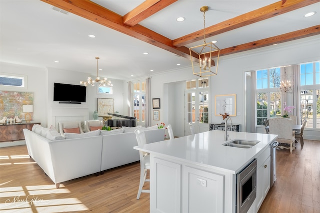 kitchen featuring a center island with sink, decorative light fixtures, white cabinetry, and beam ceiling