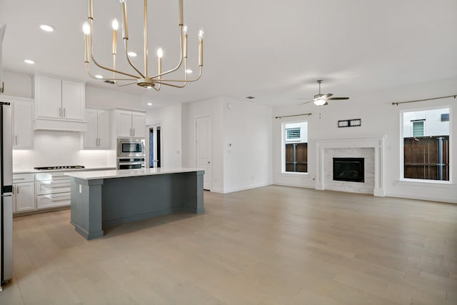 kitchen with hanging light fixtures, a kitchen island, ceiling fan with notable chandelier, white cabinets, and appliances with stainless steel finishes