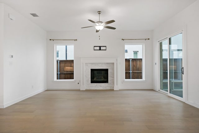 unfurnished living room with a fireplace, light wood-type flooring, ceiling fan, and a wealth of natural light