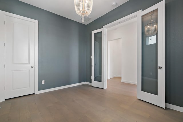 unfurnished bedroom featuring hardwood / wood-style flooring, french doors, and a chandelier