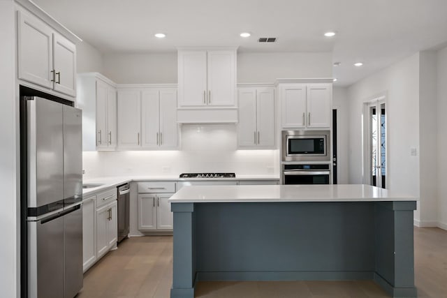 kitchen with stainless steel appliances, decorative backsplash, white cabinets, and a center island