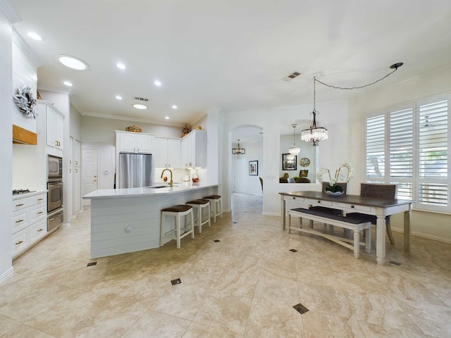 kitchen with appliances with stainless steel finishes, hanging light fixtures, kitchen peninsula, a breakfast bar, and white cabinetry